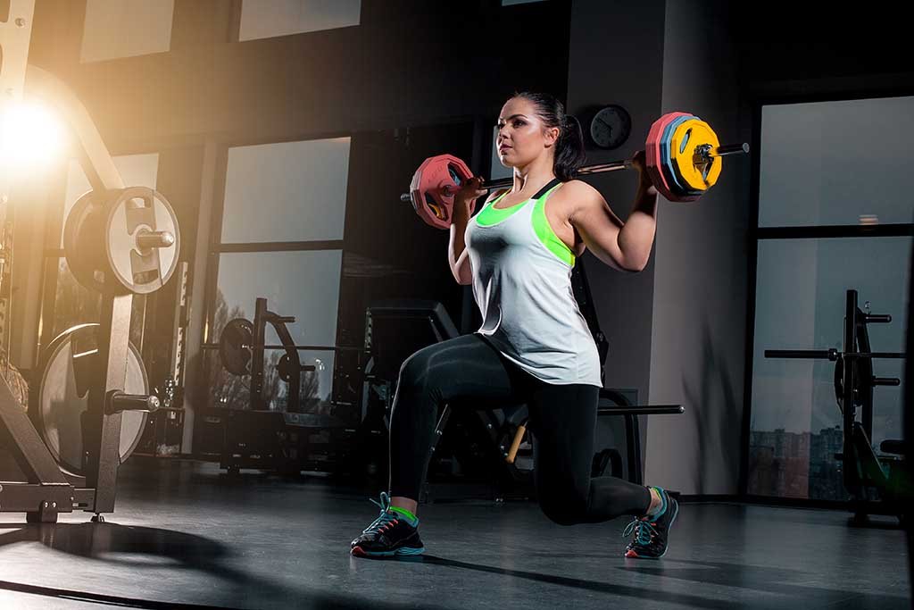 Fit young woman lifting barbells looking focused, working out in a gym